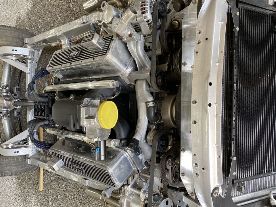 Engine block with "496" inscribed on valve cover, connected to radiator and chassis parts