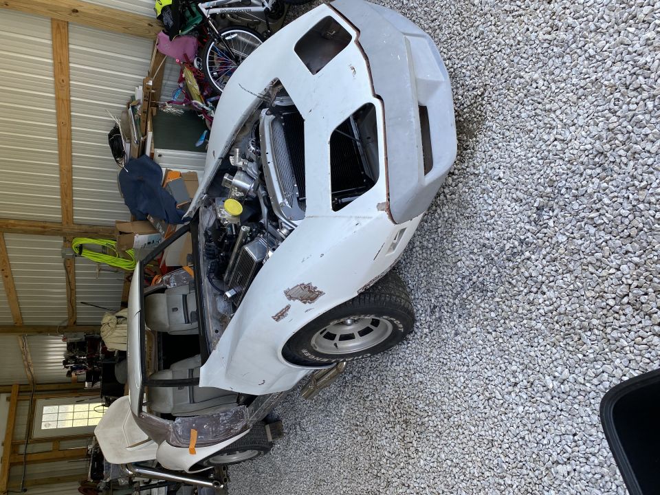 White Corvette project car in garage, hood open showing engine. Some body panels are unpainted