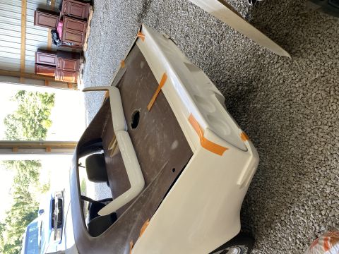 Car body with white primer and orange tape, inside a garage