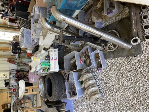 Various car parts including exhaust pipes, intake manifold, and tires piled in a garage