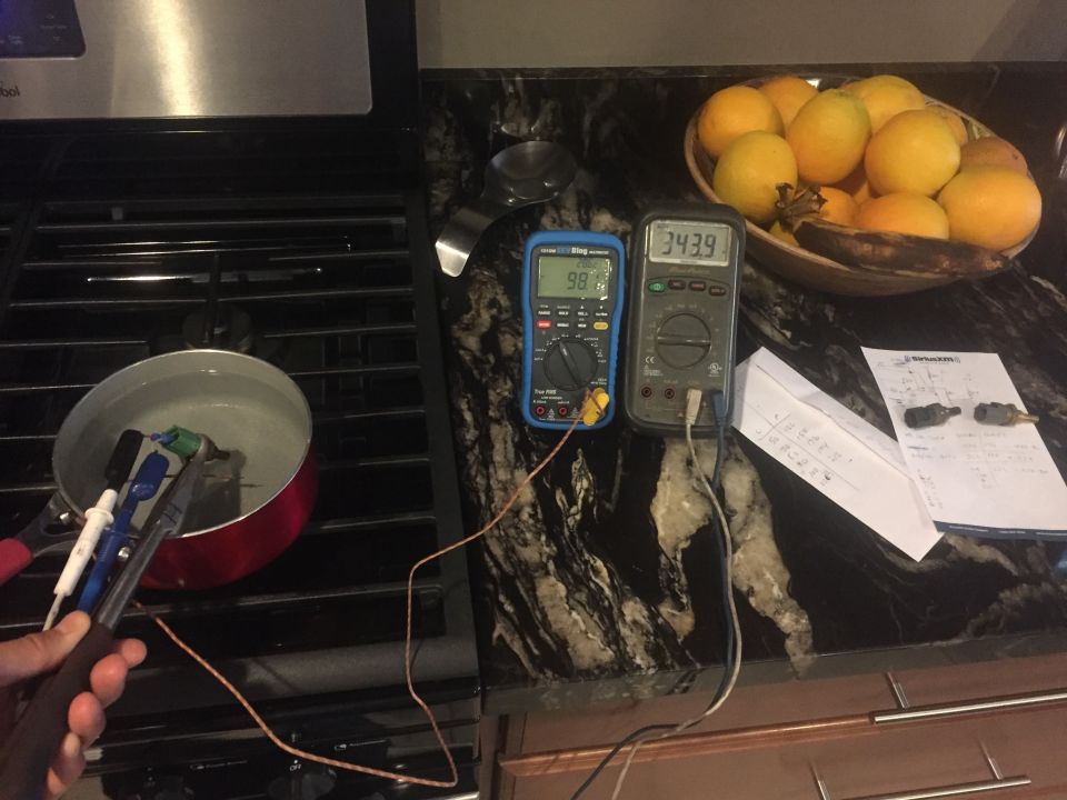 Two digital multimeters and two sensors in a pot of water on a stove