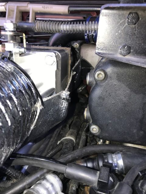 2000 Ford Explorer - A close-up view of engine components in a vehicle, featuring a silver intercooler with a hexagonal bolt, black hoses, and various metal and…