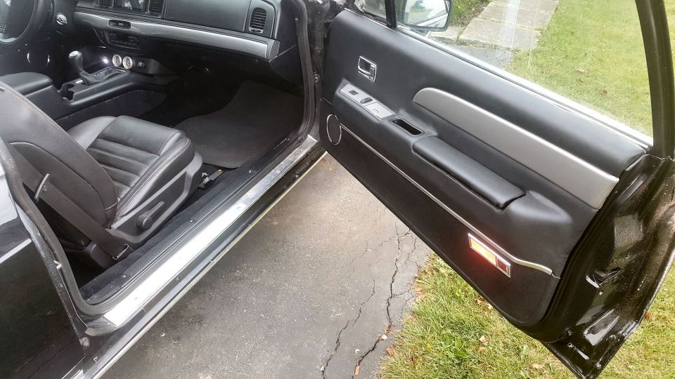 Interior view of a black sedan with the driver's door open, showing the seat, console, and door panel.