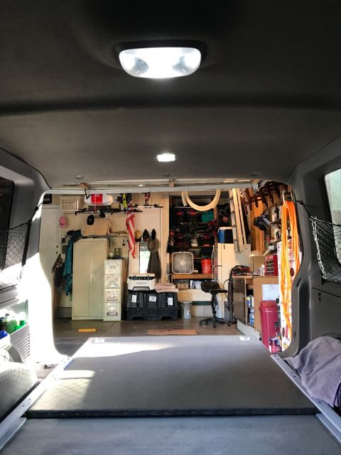 2000 Ford Explorer - Interior view of a cargo van or SUV, looking towards the open garage door. The rear cargo area is visible with storage shelves and tools in…