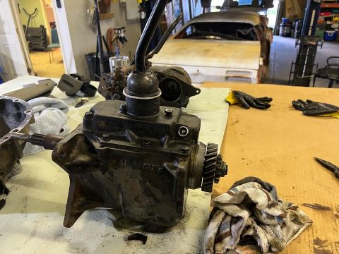 1979 Jeep CJ5 - A close-up view of a manual transmission, possibly from a Jeep CJ5, sits on a workbench next to tools and rags. The transmission is black a…