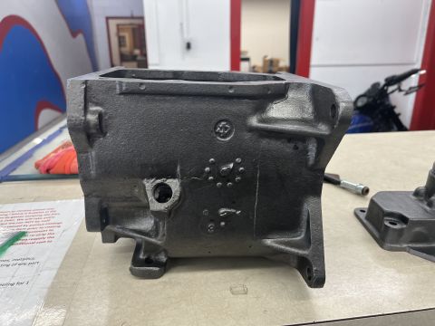 1979 Jeep CJ5 - A dark gray, cast metal automotive part, possibly a transmission housing, sits on a workbench. The part has various mounting points and a c…