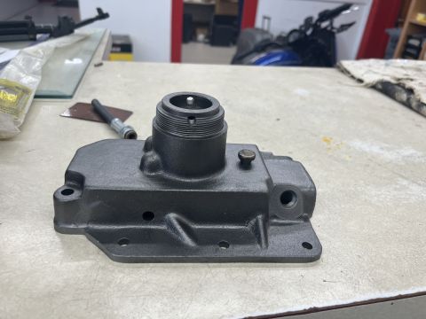 1979 Jeep CJ5 - A dark gray, cast metal automotive part with threaded sections and bolt holes sits on a textured surface. A small brass screw is visible on…