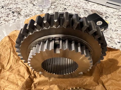 1979 Jeep CJ5 - A close-up view of two large metal gears, possibly from a transmission or differential, resting on brown paper. A set of car keys with a Vo…