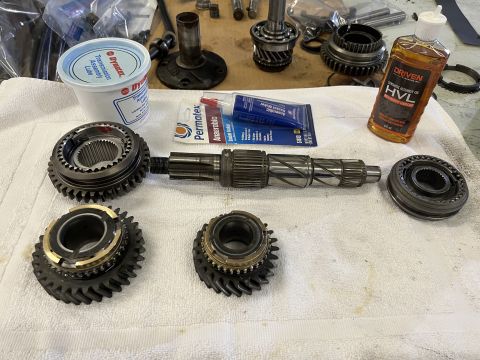 1979 Jeep CJ5 - A collection of transmission parts, including gears, a shaft, and synchronizer rings, are laid out on a white towel. A tub of assembly lube…
