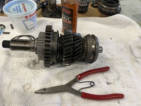 1979 Jeep CJ5 - A transmission input shaft with multiple gears and synchronizer rings is laid out on a white towel. Next to it are a tub of transmission as…