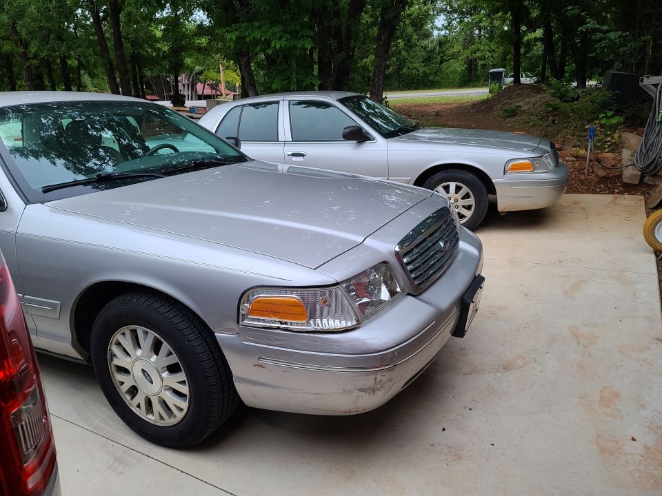 Two silver Ford Crown Victoria sedans parked on a concrete driveway.