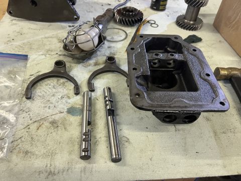 1979 Jeep CJ5 - A workbench displays disassembled Jeep CJ5 transmission parts including shift forks, selector shafts, and a transmission case. A work light…