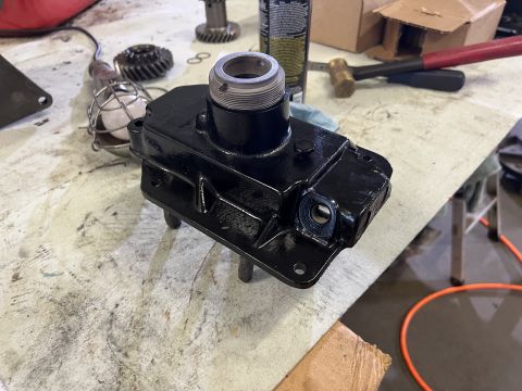 1979 Jeep CJ5 - A black painted automotive part, possibly a transmission or transfer case housing, sits on a workbench with various tools and gears in the…