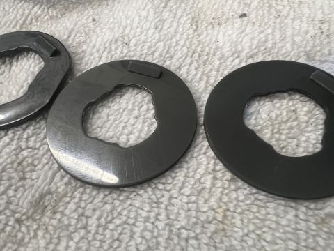 1979 Jeep CJ5 - Three metal washers with irregular inner edges and a small rectangular tab on the outer edge are laid out on a white textured surface.
