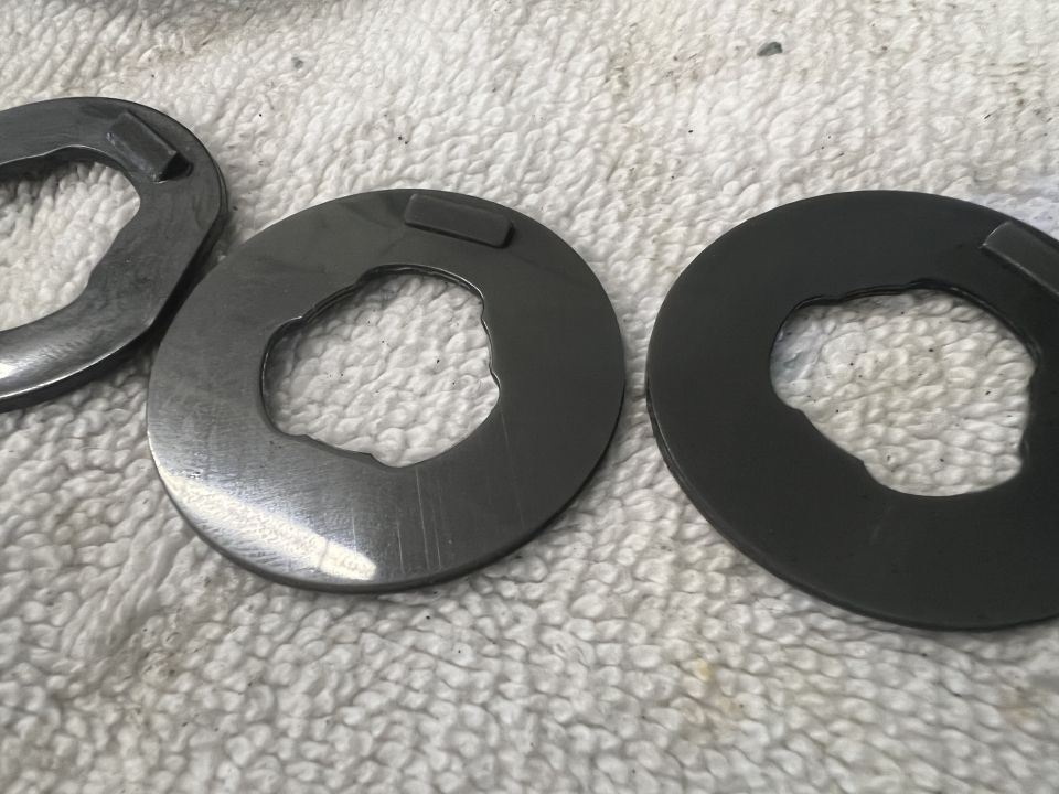 Three metal washers with irregular inner edges and a tab on a white textured surface.