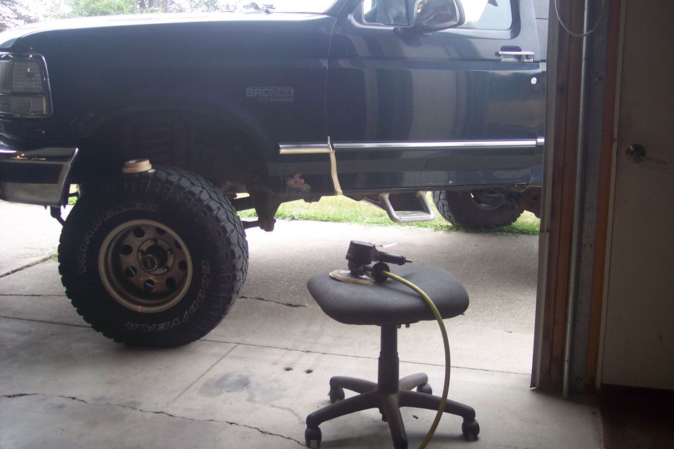 Dark colored SUV with "BRONCO" badging, parked in a garage, with a sander on a stool.
