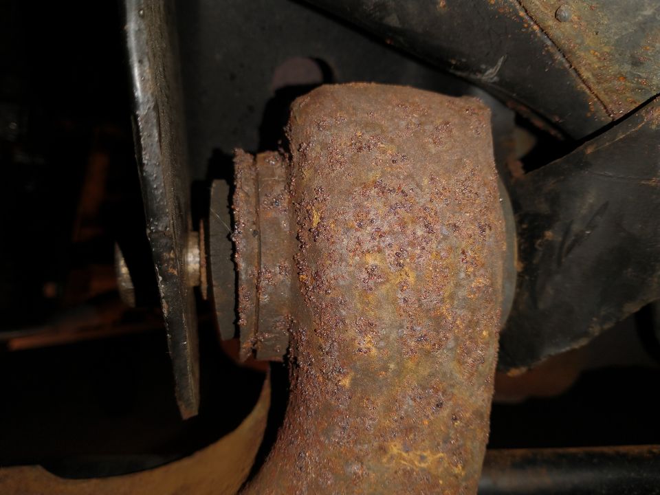 Close-up of a heavily rusted suspension component, possibly a control arm bushing mount