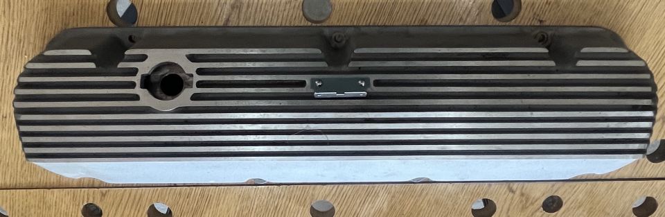 Aluminum finned valve cover with horizontal fins and a circular opening on the left.