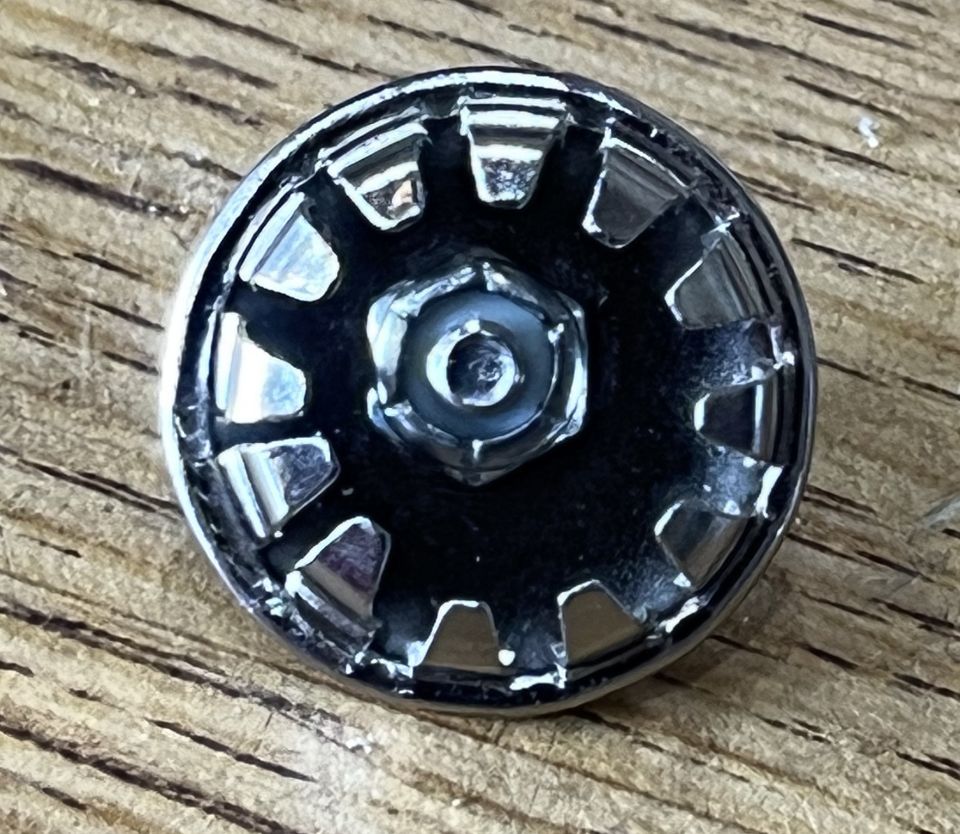 Chrome lug nut with black center and starburst pattern on wood
