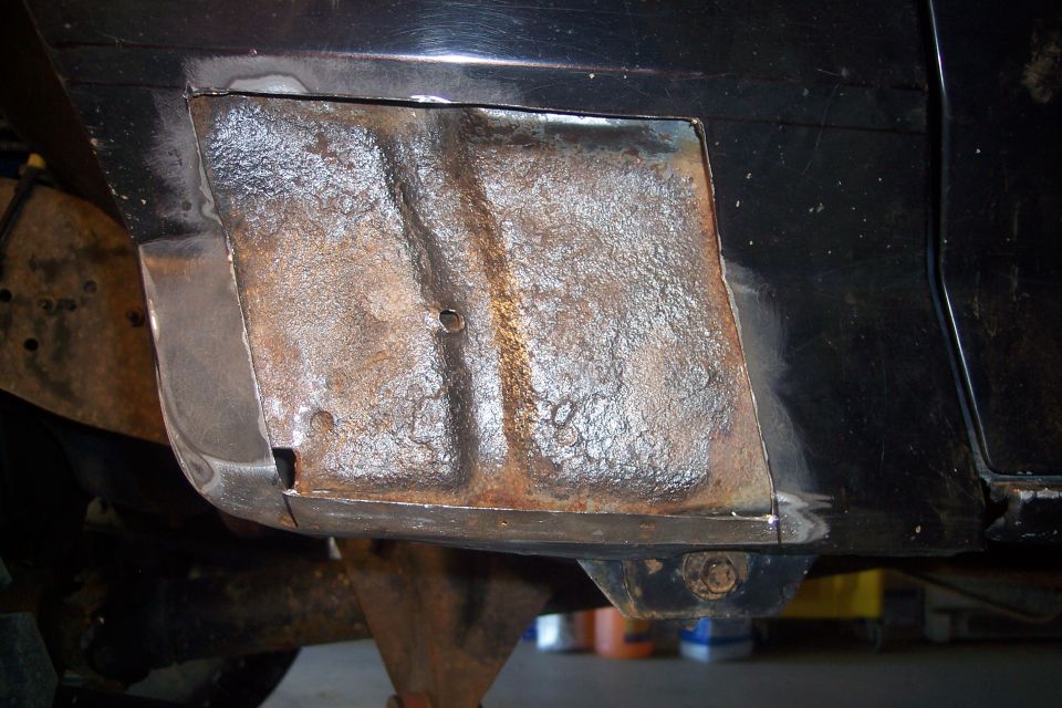 Close-up of rusted metal repair on a black vehicle body panel.
