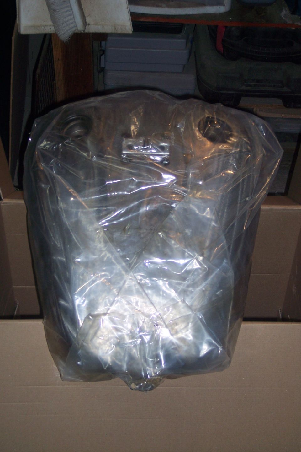 Silver motorcycle fuel tank wrapped in plastic inside a box.