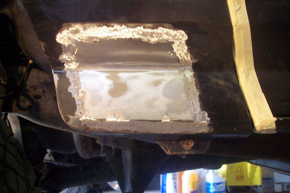 close-up of rust repair on a vehicle's lower body panel, showing metalwork and primer