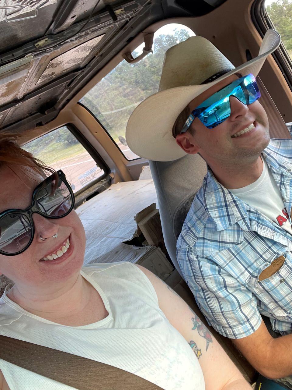 Two people in the interior of a vehicle, one wearing a cowboy hat and sunglasses