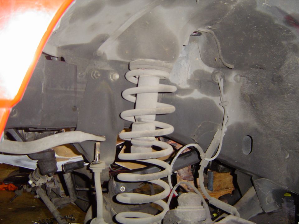 Front coil spring and suspension under an orange vehicle wheel well