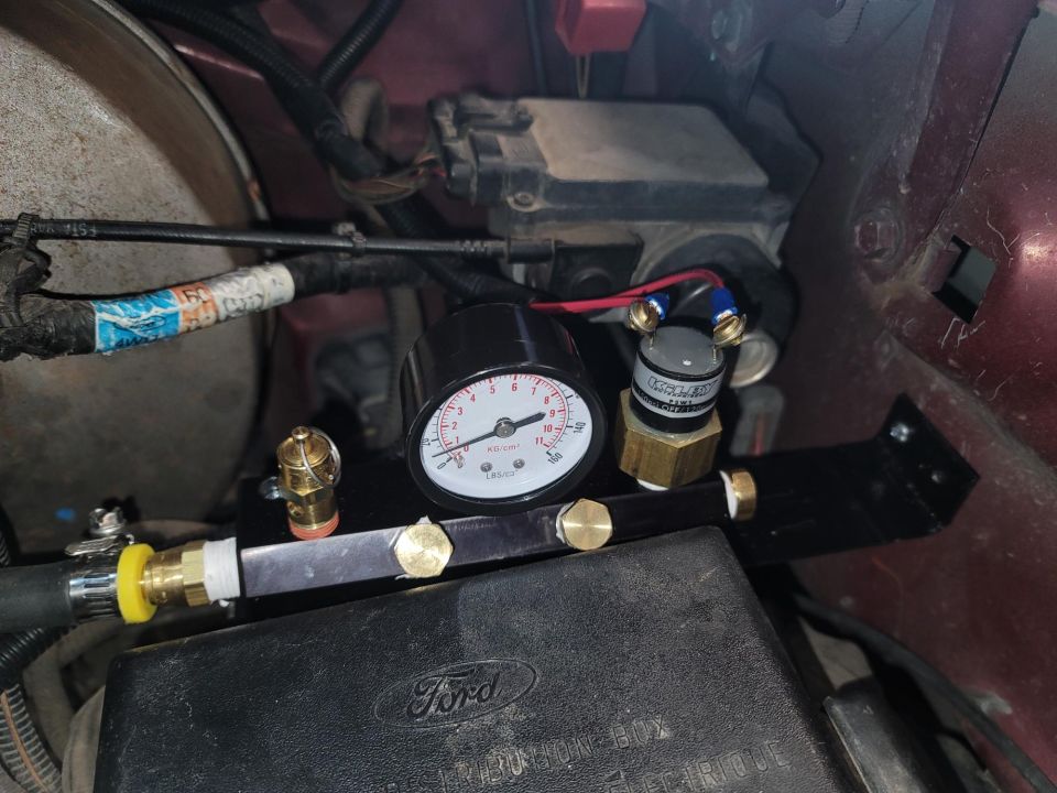 Close-up of an on-board air system gauge and brass fittings mounted near a Ford fuse box
