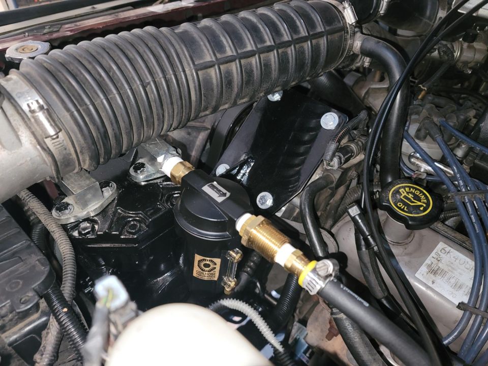 Engine bay with black air compressor, hoses, and air intake tube. Visible text includes "ENGINE OIL" and "SUPERMOTORS.NET"