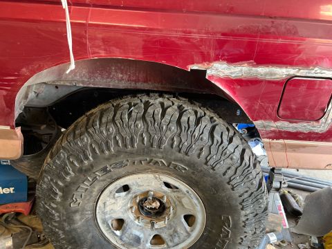 1995 Ford Bronco - The rear fender of a red SUV shows signs of repair and modification, with a large tire in place.