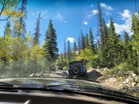 1996 Ford Bronco - Multiple SUVs navigate a challenging rocky trail through a forest on a sunny day. A Supermotors.net logo is visible.