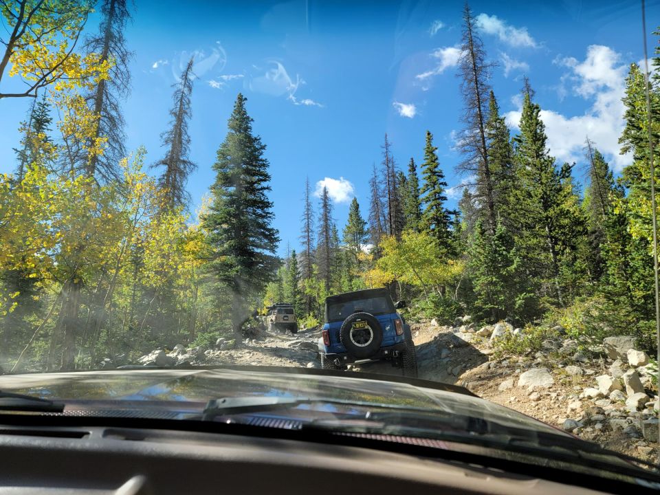 Blue SUV on rocky mountain road, rear view. Supermotors.net logo visible
