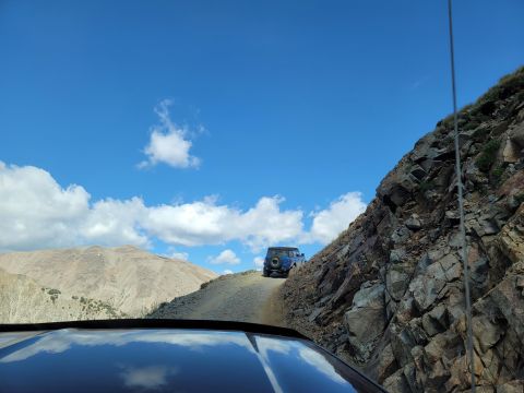 1996 Ford Bronco - Two off-road vehicles navigate a steep, winding dirt path on a mountainside.