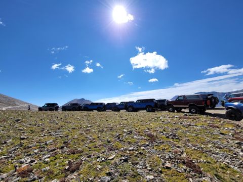1996 Ford Bronco - A group of SUVs are parked on a rocky hillside with mountains in the background and a bright sun overhead.