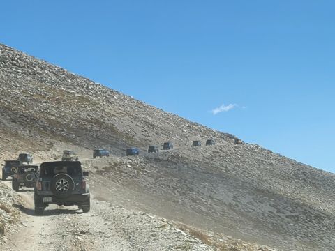 1996 Ford Bronco - A line of Jeeps navigates a steep, unpaved mountain trail on a sunny day.