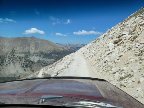 1996 Ford Bronco - View from inside a vehicle driving on a narrow, rocky mountain road under a blue sky.