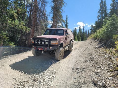 1996 Ford Bronco - This 1996 Ford Bronco is navigating a challenging off-road trail in a wooded mountain area.