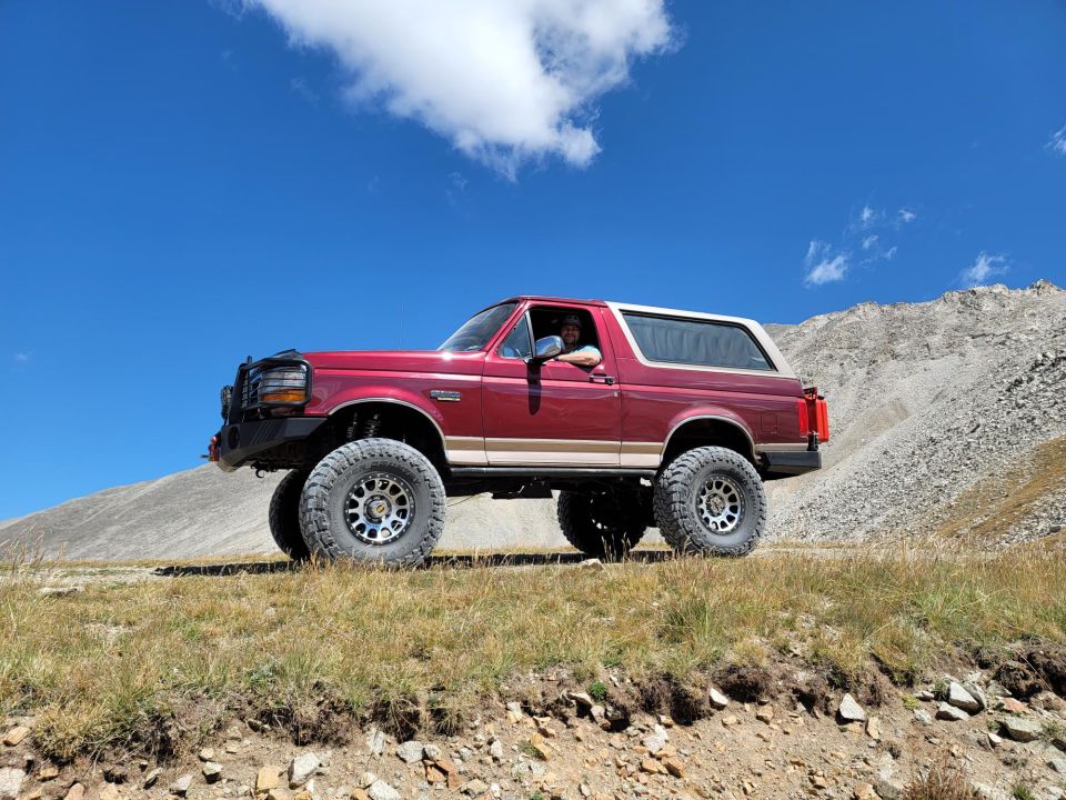 Red 1992 Ford Bronco with tan top and aftermarket wheels on a dirt road