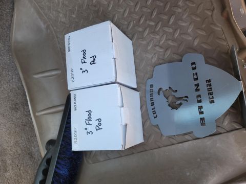 1996 Ford Bronco - Boxes of flood pods and a Bronco-themed metal plate are visible on the floor of a vehicle.