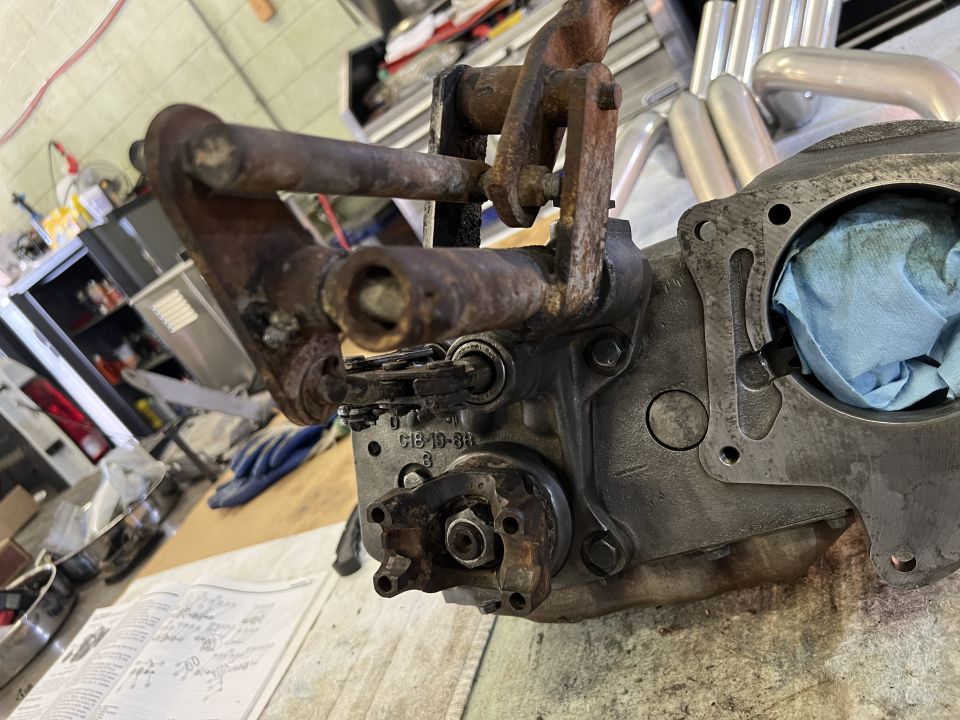Rusty metal linkage attached to a gray engine block with blue cloth stuffed inside
