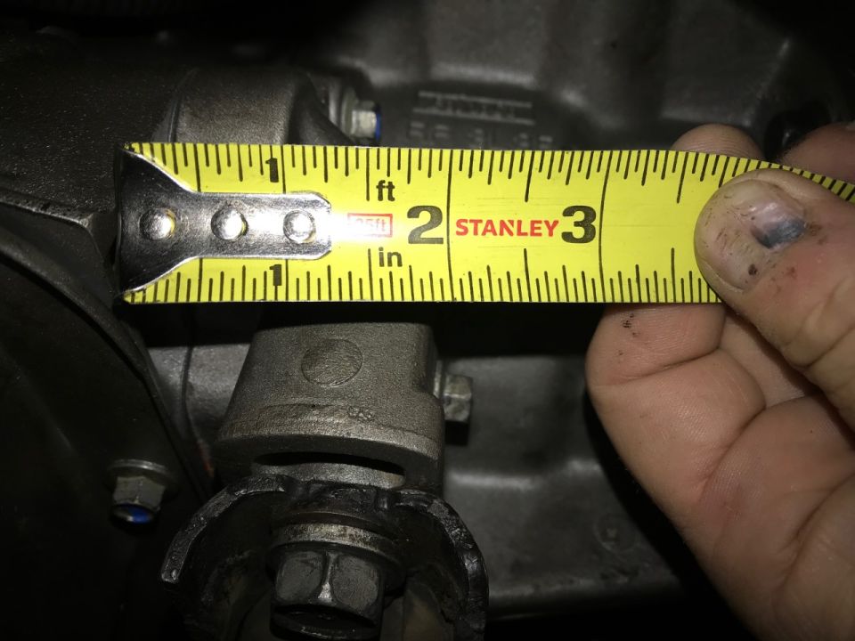 Close-up of a metal transmission component being measured with a yellow Stanley tape measure