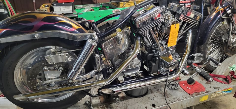 Motorcycle engine and rear wheel with flame graphics on the fender. It's on a workbench with tools
