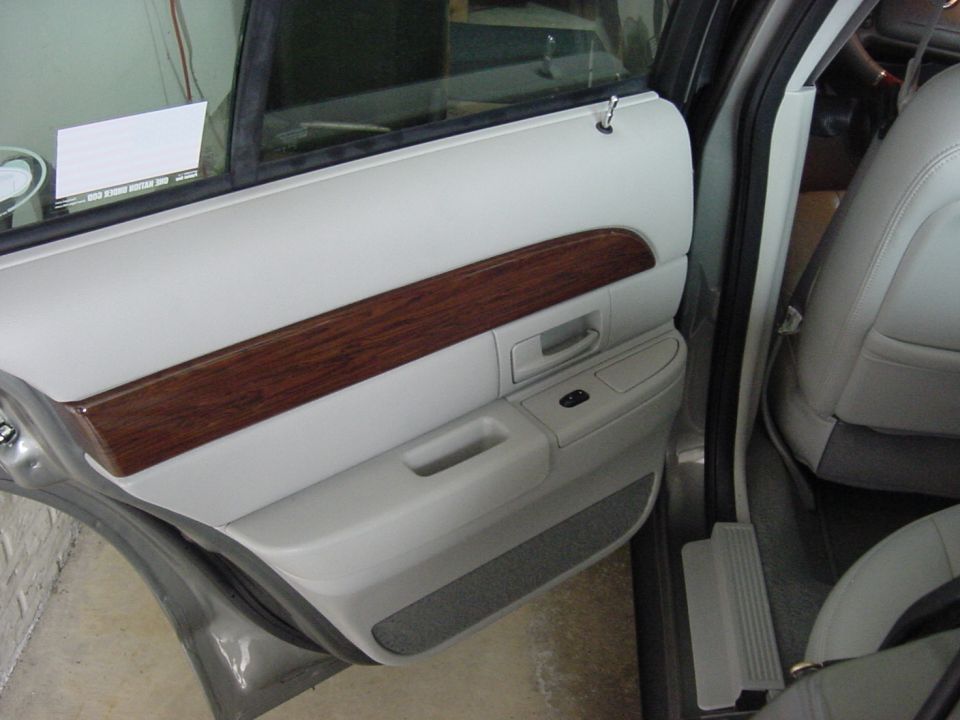 Rear door panel of a grey sedan with woodgrain trim, chrome handle and grey seats