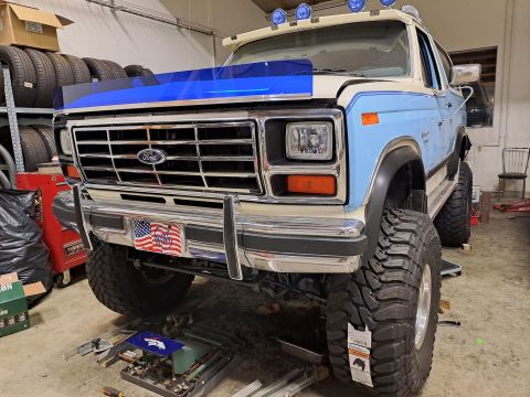 1996 Ford Bronco - This lifted Ford Bronco features a prominent chrome grille and a two-tone blue and white paint scheme.