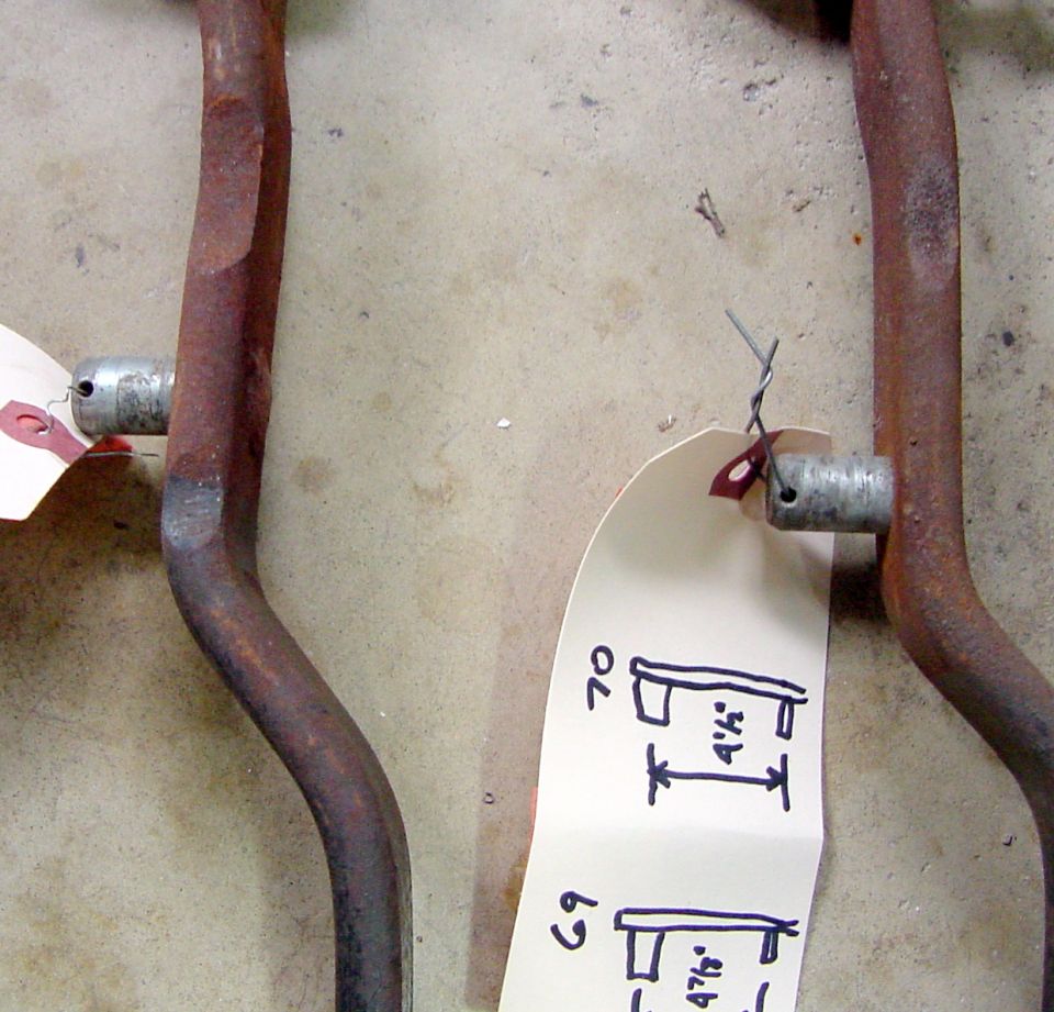 Two rusty linkage rods with measurement tags, one labeled '70' and '4 1/4"'