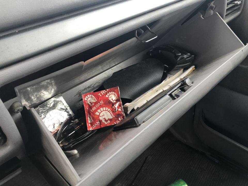 Open glove compartment with a Trojan condom package, foil-wrapped item, and other objects inside