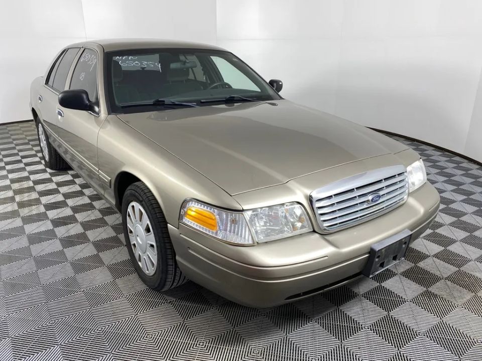 Tan Ford Crown Victoria with a chrome grille and amber turn signals. VIN and other markings are visible on the windshield