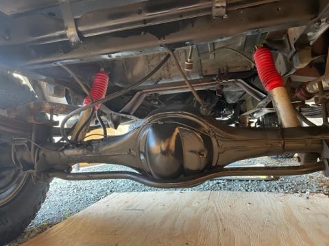 1978 Ford Bronco - Underside view of a vehicle's rear axle and suspension system, showing red shock absorbers and leaf springs.