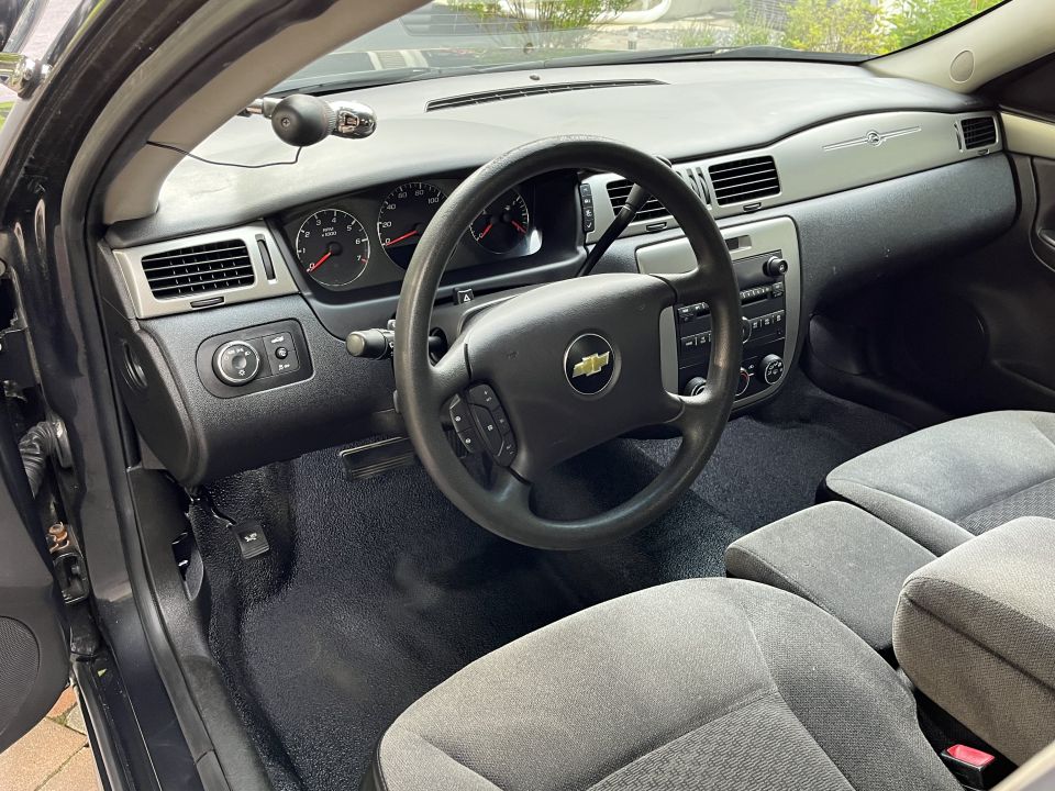 Car interior showing dashboard, steering wheel, seats, and a device on the windshield.